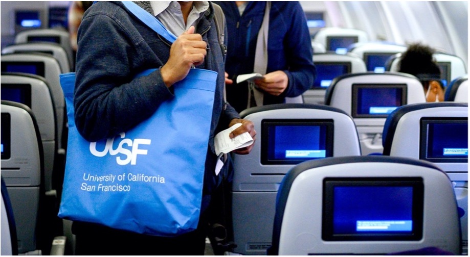 A traveler holding a UCSF tote bag while finding a seat on an airplane